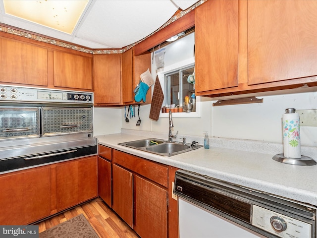 kitchen with a sink, brown cabinetry, white dishwasher, stainless steel oven, and light countertops