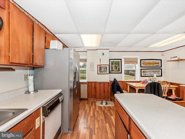 kitchen with a drop ceiling, wainscoting, brown cabinets, light wood-style floors, and white dishwasher