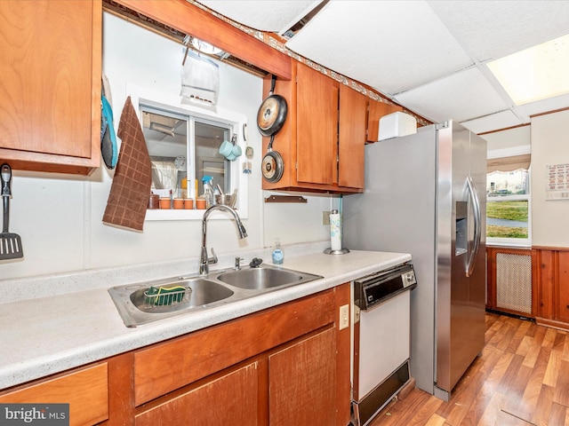 kitchen featuring a sink, brown cabinetry, light wood finished floors, dishwasher, and light countertops