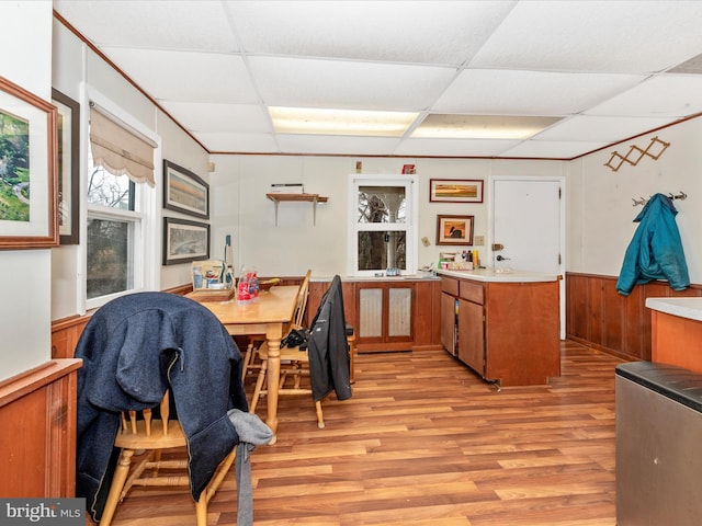 dining area with a paneled ceiling, light wood-type flooring, and wainscoting