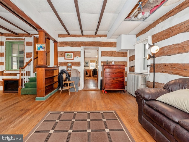 living area with stairway, beam ceiling, radiator, and wood finished floors