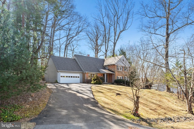 view of front facade featuring a garage, roof with shingles, a chimney, and aphalt driveway