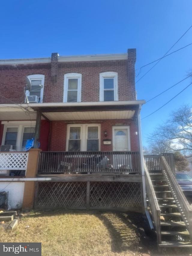 view of front facade featuring covered porch, brick siding, and stairs