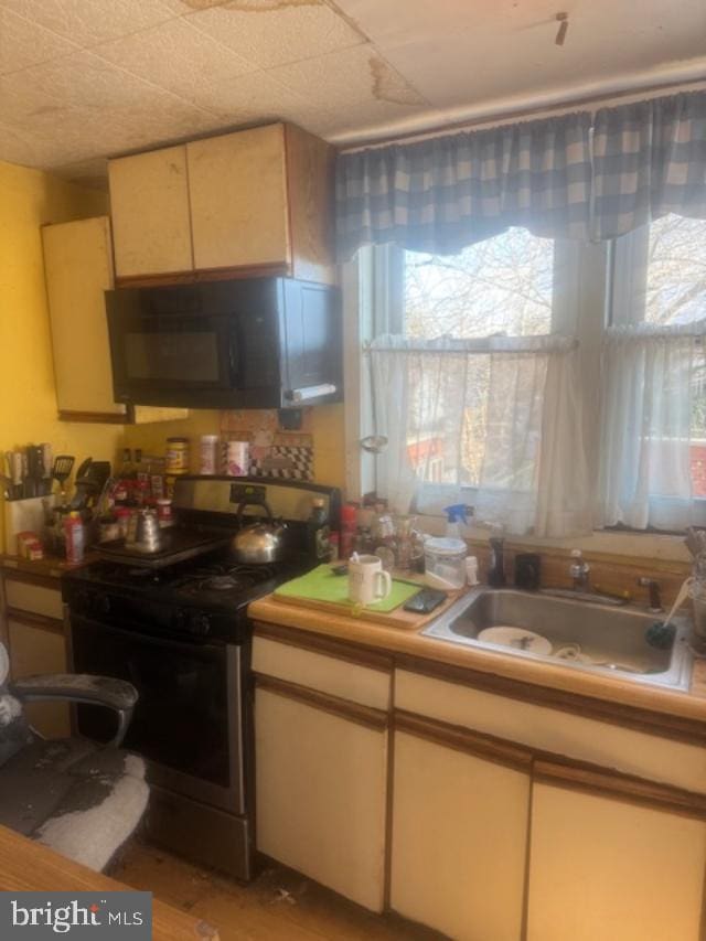 kitchen featuring black microwave, light countertops, stainless steel gas range oven, and a sink