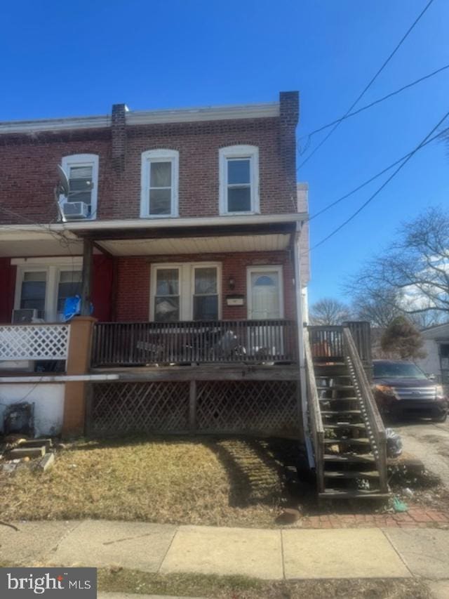 view of property with covered porch, brick siding, and stairs