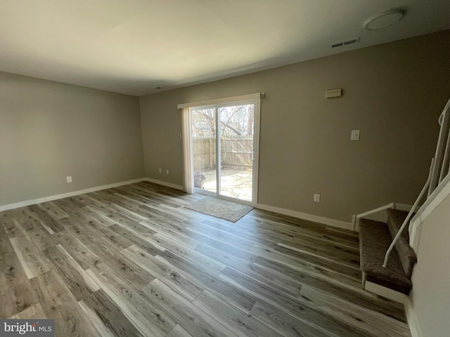 unfurnished living room featuring visible vents, baseboards, wood finished floors, and stairway