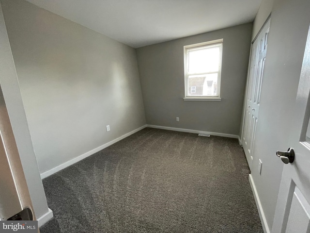 unfurnished bedroom with baseboards, dark colored carpet, and a closet