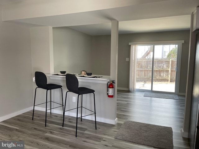 kitchen featuring a kitchen breakfast bar, a peninsula, baseboards, and wood finished floors