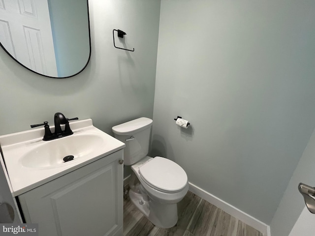 half bathroom featuring toilet, vanity, baseboards, and wood finished floors