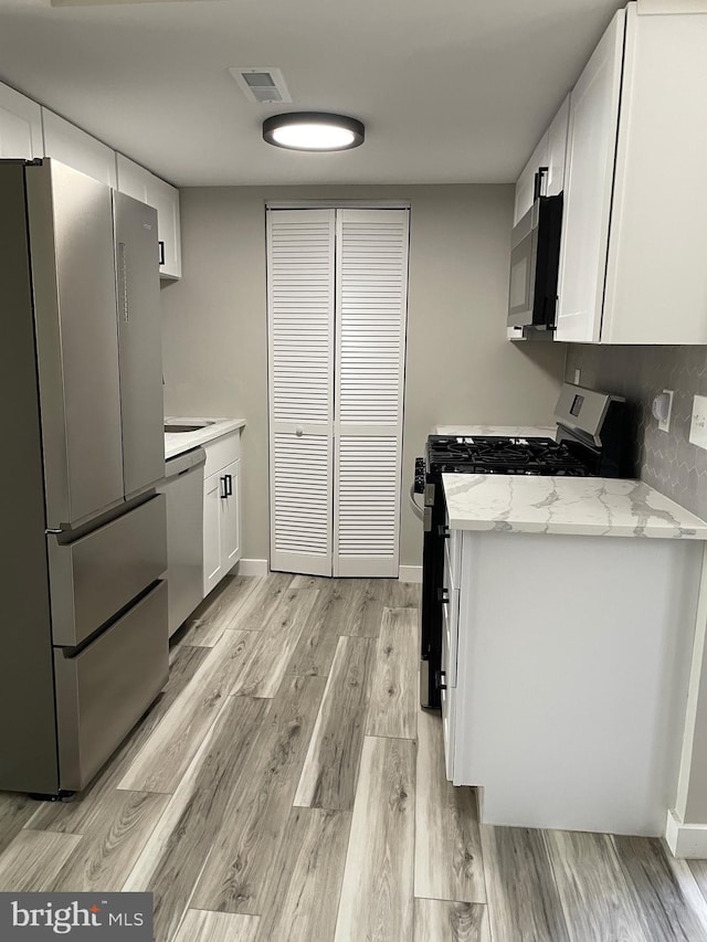 kitchen featuring light wood finished floors, visible vents, light stone counters, appliances with stainless steel finishes, and white cabinets