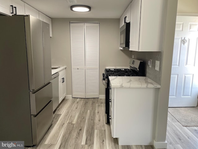 kitchen with light wood-style flooring, light stone counters, backsplash, stainless steel appliances, and white cabinets