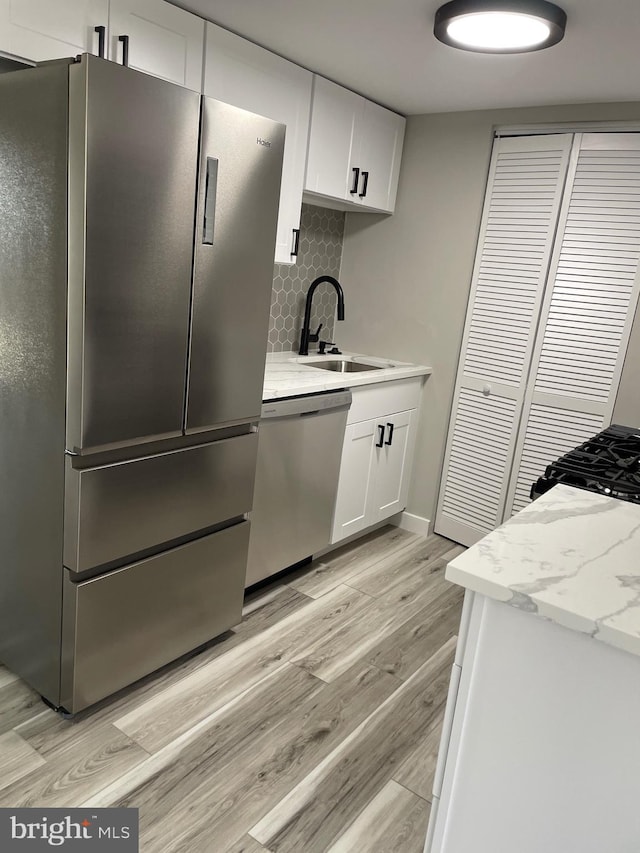 kitchen featuring light wood-style flooring, a sink, tasteful backsplash, white cabinetry, and appliances with stainless steel finishes