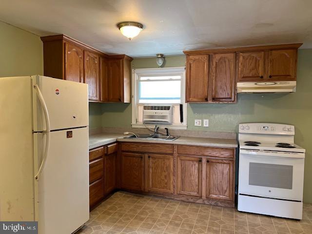 kitchen with under cabinet range hood, light countertops, brown cabinetry, white appliances, and a sink