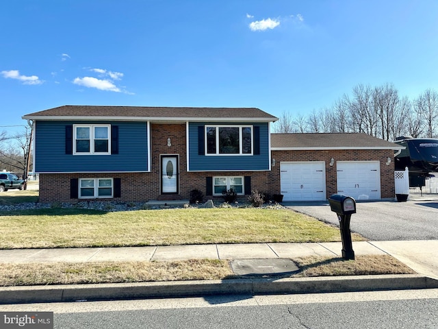 split foyer home with a garage, aphalt driveway, a front lawn, and brick siding