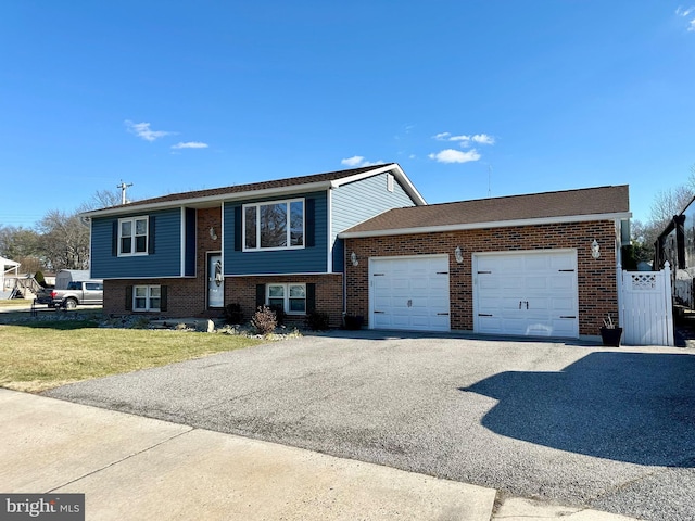 bi-level home with an attached garage, driveway, a front lawn, and brick siding