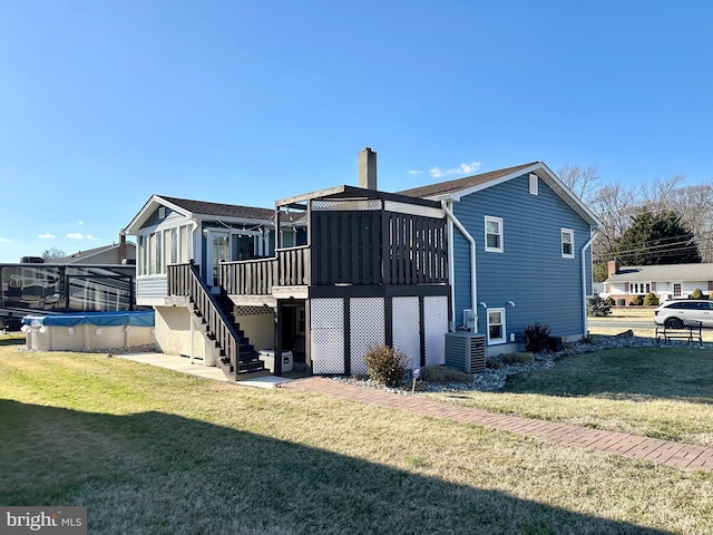 rear view of house with a covered pool, a chimney, stairs, a deck, and a yard