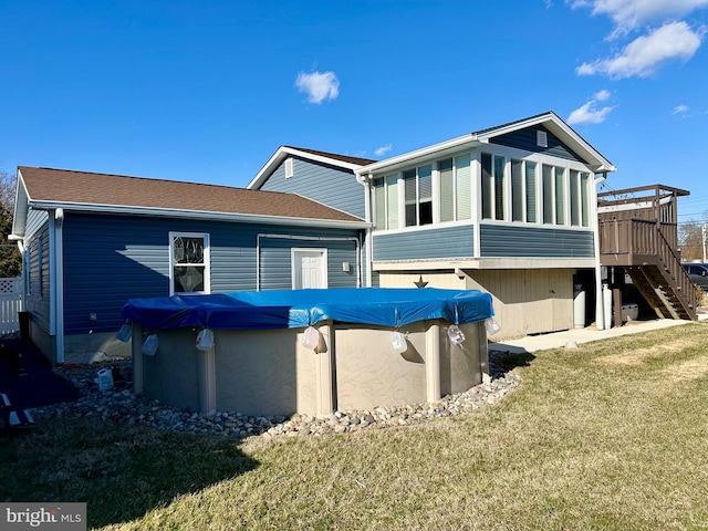 rear view of property featuring stairs, a lawn, a wooden deck, and a covered pool