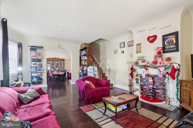 living room featuring baseboards, arched walkways, wood finished floors, and stairs