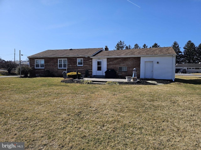 rear view of property featuring a patio area, a lawn, brick siding, and a chimney