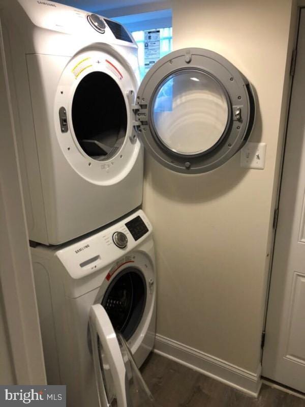 washroom featuring stacked washer and dryer, dark wood finished floors, laundry area, and baseboards