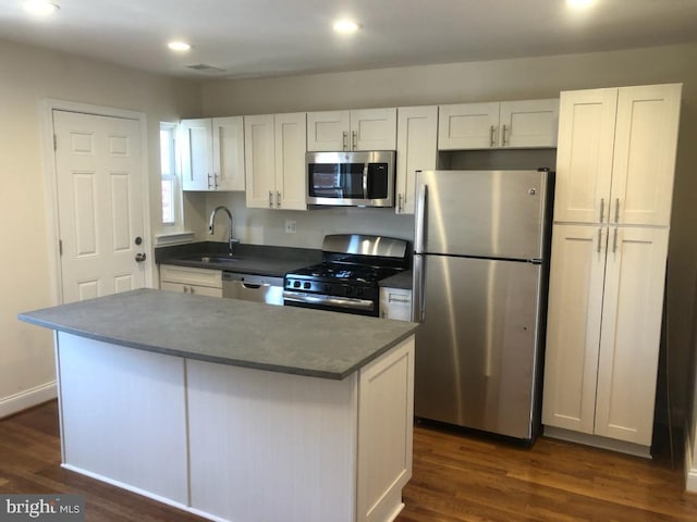 kitchen featuring stainless steel appliances, dark wood-style flooring, a sink, white cabinets, and dark countertops