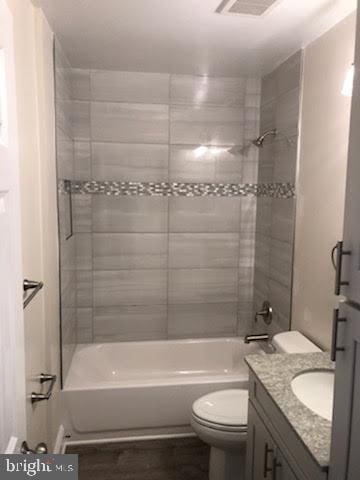 bathroom featuring visible vents, toilet, wood finished floors, tub / shower combination, and vanity