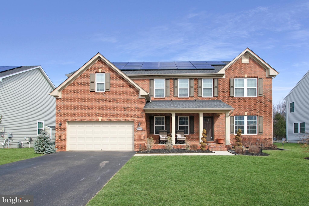 view of front facade with driveway, brick siding, a front yard, and roof mounted solar panels