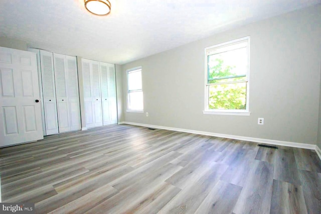 unfurnished bedroom with baseboards, multiple closets, visible vents, and wood finished floors