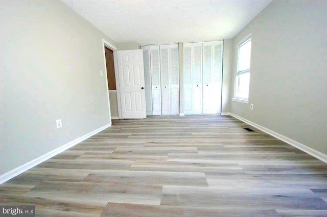 unfurnished bedroom featuring visible vents, baseboards, multiple closets, and wood finished floors