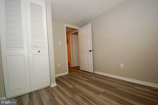 unfurnished bedroom featuring wood finished floors, baseboards, and a closet