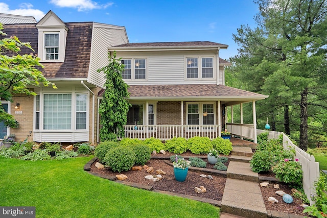 view of front facade featuring a porch, fence, roof with shingles, a front yard, and brick siding