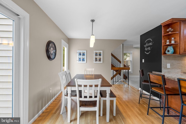 dining area with light wood finished floors, stairway, and baseboards