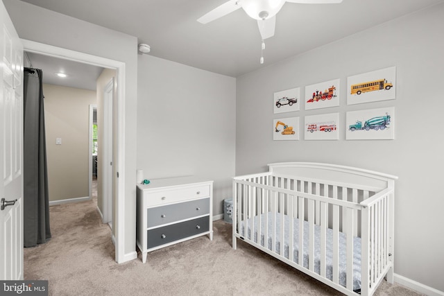 carpeted bedroom featuring a crib, a ceiling fan, and baseboards