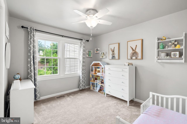 bedroom featuring visible vents, a nursery area, carpet flooring, baseboards, and ceiling fan