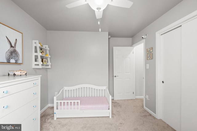 unfurnished bedroom with a crib, baseboards, ceiling fan, light colored carpet, and a closet