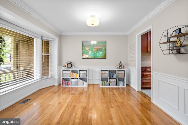 recreation room featuring crown molding, wainscoting, visible vents, and light wood-type flooring