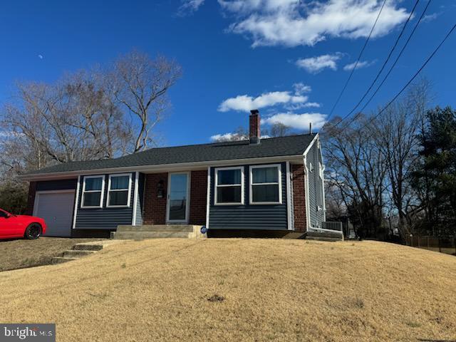 single story home featuring an attached garage, a front yard, a chimney, and brick siding