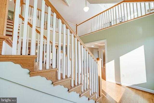 stairway featuring a high ceiling, baseboards, and wood finished floors