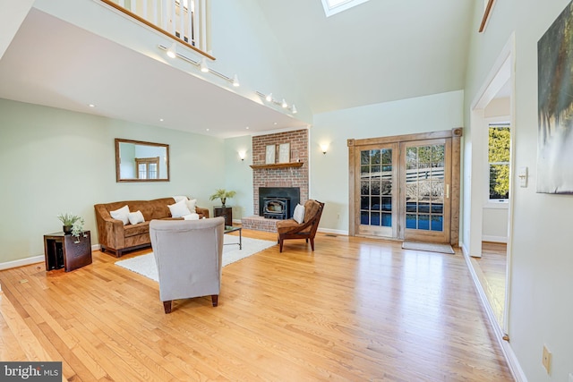 living room with baseboards, a skylight, light wood-style floors, a towering ceiling, and a brick fireplace