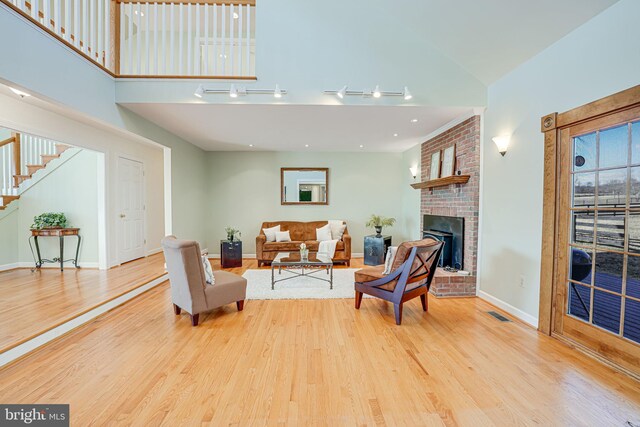 living area featuring a brick fireplace, a high ceiling, and wood finished floors