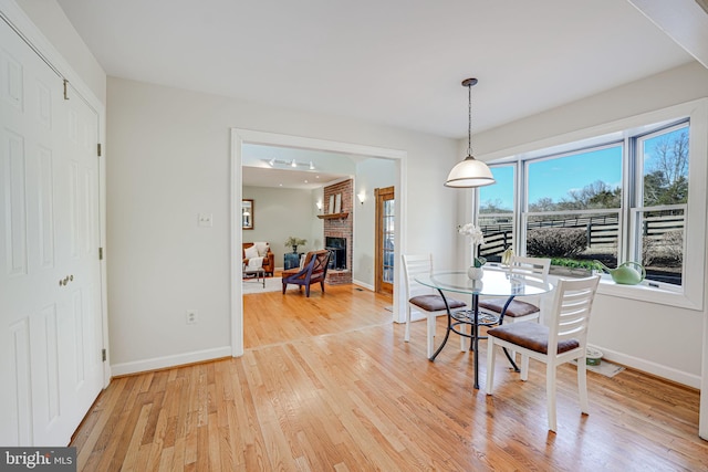 dining room featuring a brick fireplace, baseboards, and light wood-style floors