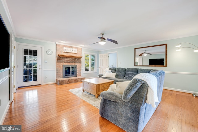 living room with ceiling fan, hardwood / wood-style flooring, a brick fireplace, and ornamental molding