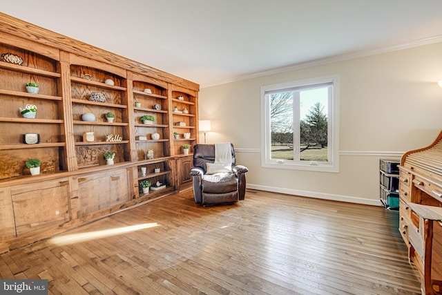 sitting room with baseboards, wood-type flooring, and ornamental molding