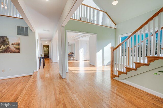 entryway with stairway, wood finished floors, baseboards, visible vents, and high vaulted ceiling