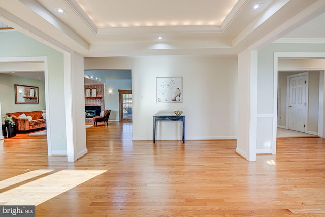 interior space with a raised ceiling, a brick fireplace, crown molding, and light wood finished floors