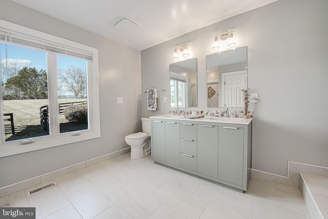 full bathroom with visible vents, baseboards, toilet, double vanity, and a sink