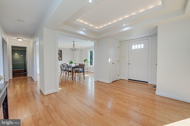 entryway with an inviting chandelier, a tray ceiling, baseboards, and light wood-type flooring