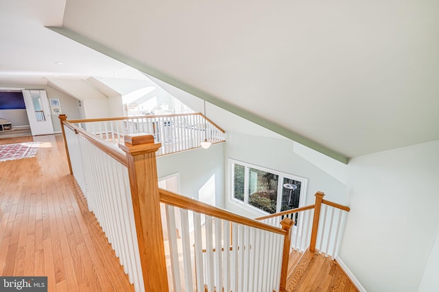 hall featuring lofted ceiling, light wood-style flooring, and an upstairs landing