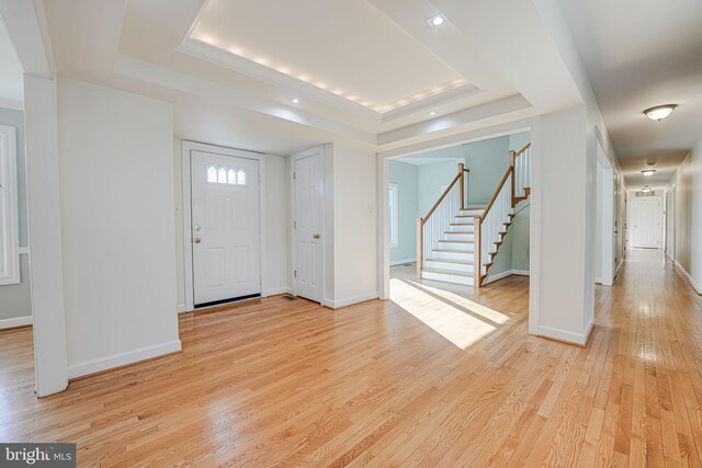 entrance foyer with baseboards, stairs, a raised ceiling, and light wood-style floors