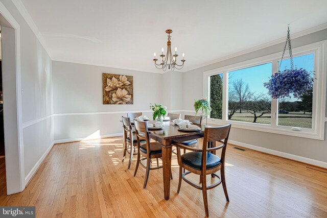 dining space with baseboards, visible vents, light wood-style flooring, ornamental molding, and a notable chandelier